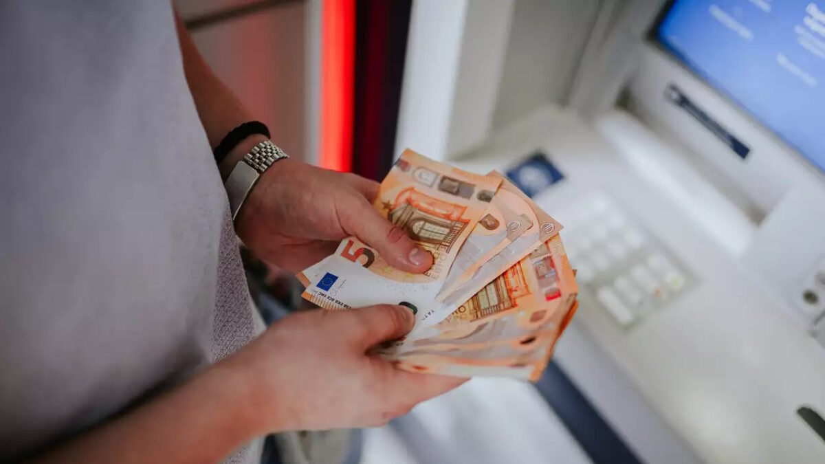 A person holding euro banknotes infront of an atm