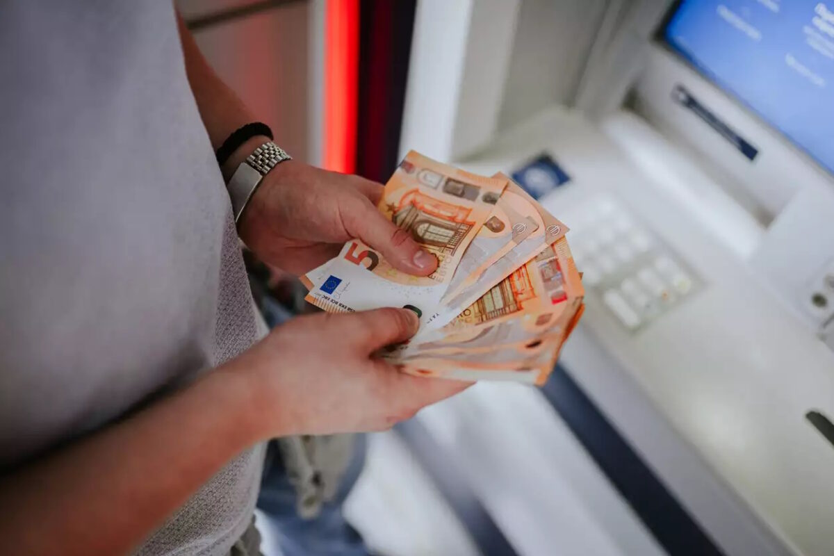 A person holding euro banknotes infront of an atm