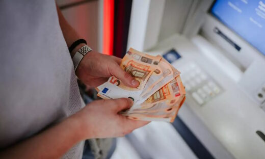 A person holding euro banknotes infront of an atm