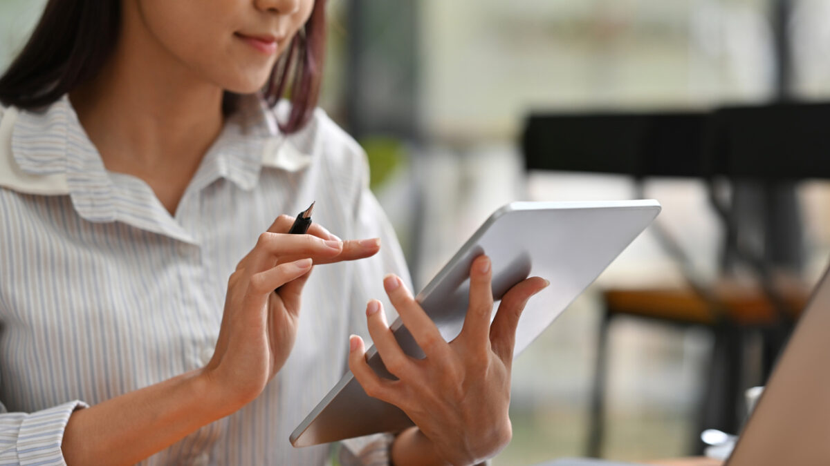 Close up image of a woman using a tablet infront of a laptop