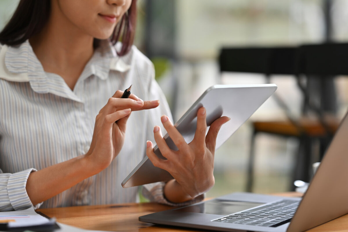 Close up image of a woman using a tablet infront of a laptop