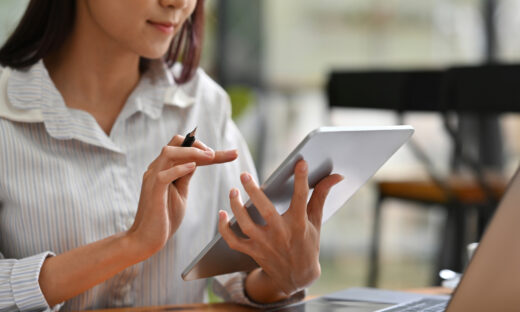 Close up image of a woman using a tablet infront of a laptop