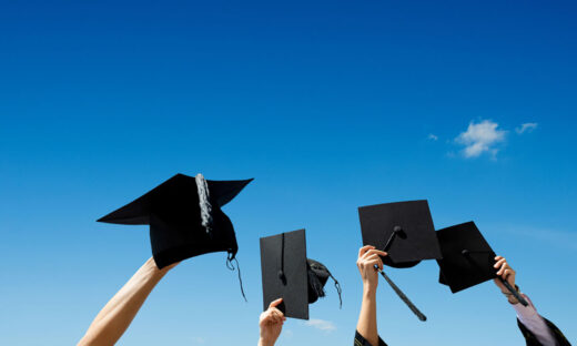 Four hands holding graduation hats against blue sky