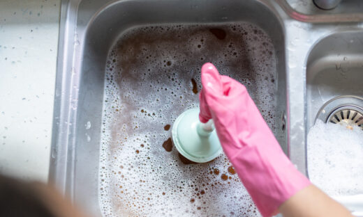 Woman Using Plunger In Blocked Kitchen Sink To Unclog Drain