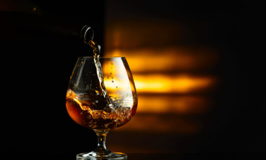 Pouring brandy from a bottle into a snifter on a black reflective background. Copy space.