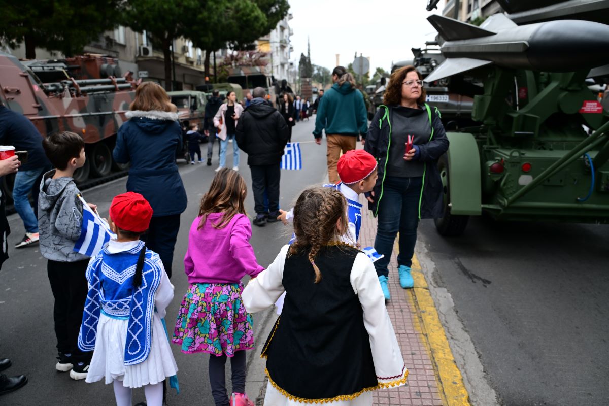 Παιδάκια με παραδοσιακές στολές και ελληνικές σημαίες περιεργάζονται με δέος τα στρατιωτικά οχήματα πριν την έναρξη της στρατιωτικής παρέλασης