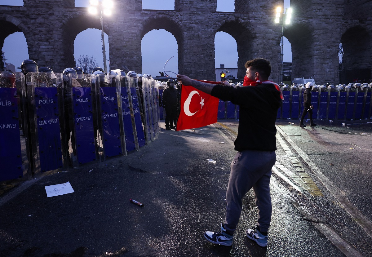 A person holds a Turkish flag as police officers stand guard during a protest on the day Istanbul Mayor Ekrem Imamoglu was jailed as part of a corruption investigation, in Istanbul, Turkey, March 23, 2025. REUTERS