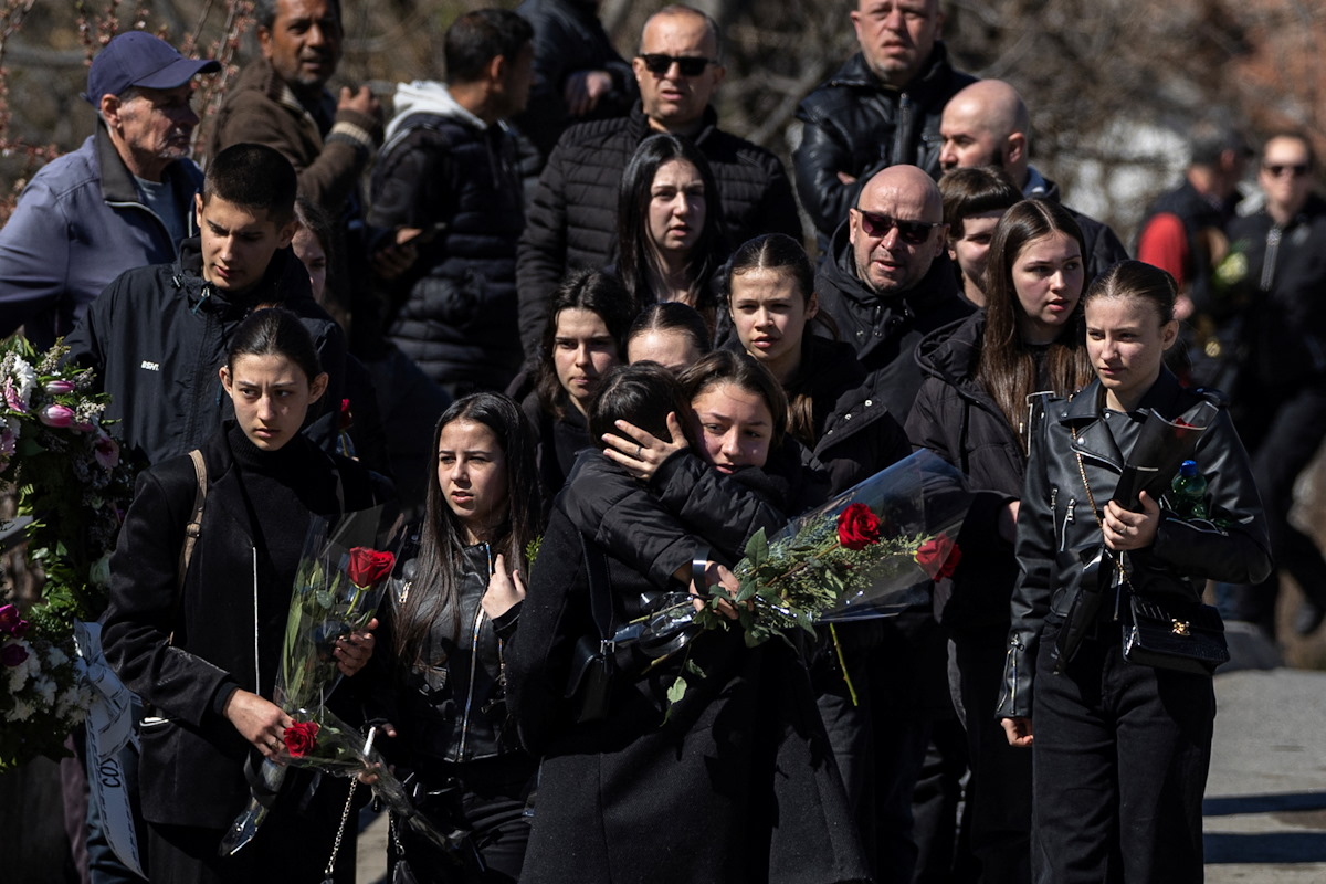 Συγγενείς θυμάτων αγκαλιάζονται έχοντας λουλούδια στα χέρια τους